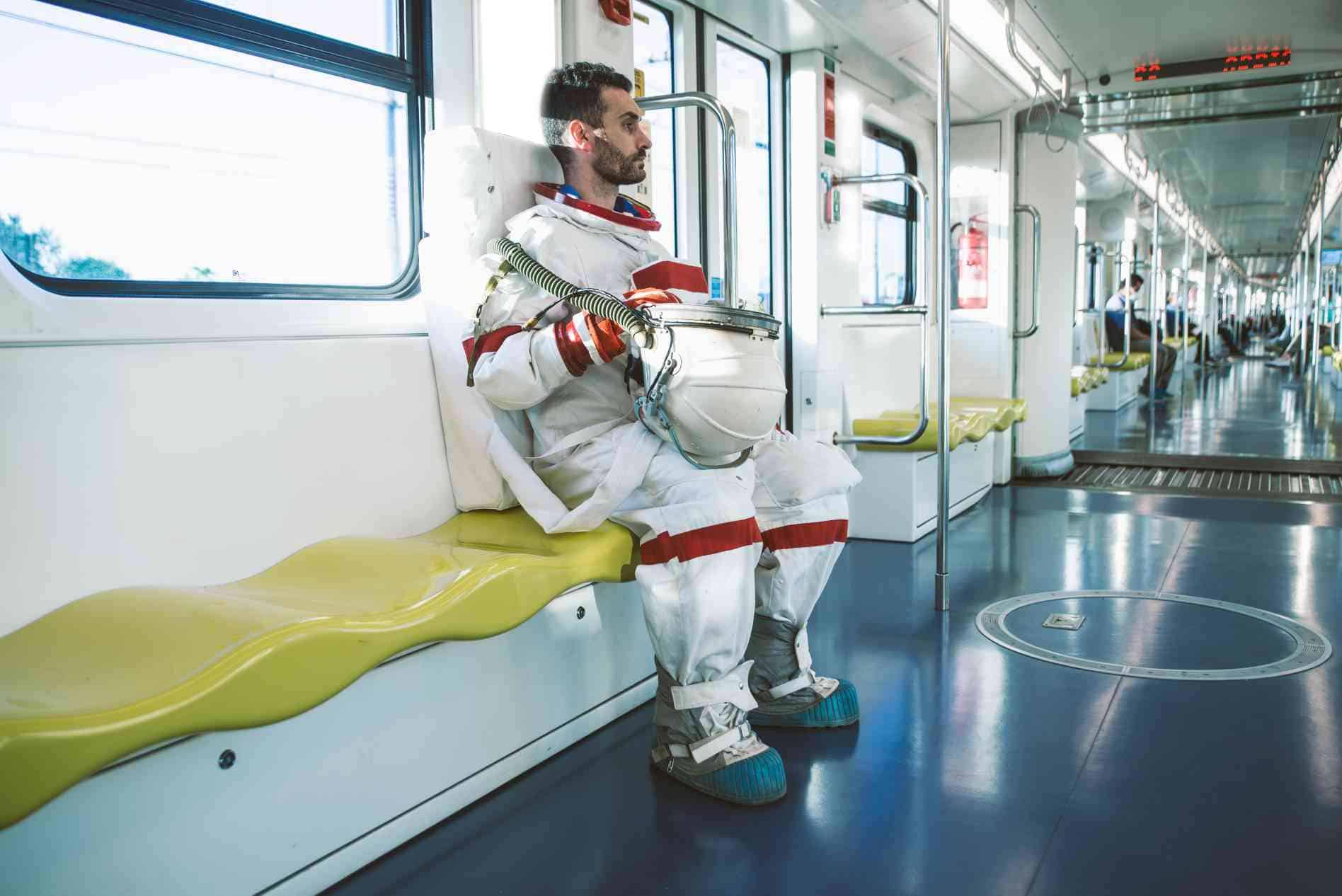 spaceman sitting on an empty metro with his helmet in his hands